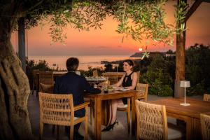 a man and a woman sitting at a table in front of a sunset at Cap St Georges Hotel & Resort in Peyia