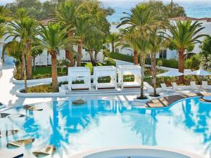 een zwembad met witte stoelen en palmbomen bij Caramel Grecotel Boutique Resort in Adelianos Kampos