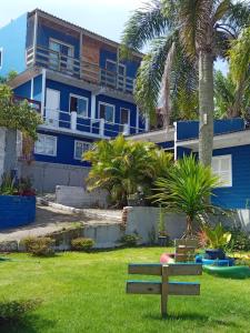 a blue house with palm trees and a bench at Hospedaria Mirante da maré ap2 in Imbituba