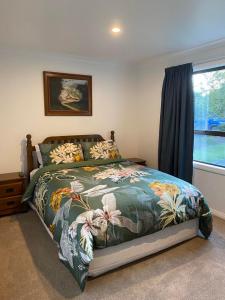 a bedroom with a bed with a floral bedspread and a window at Kereru Cottage in Kaikoura