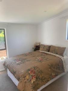 a white bedroom with a bed with a floral bedspread at Kereru Cottage in Kaikoura