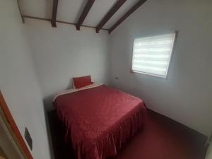 Habitación con cama con colcha roja y ventana. en Cabaña la estancia, en La Estancia