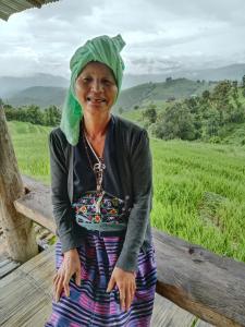 an older woman sitting on a bench with a green hat on her head at บ้านพักชิปู ป่าบงเปียง in Ban Mae Pan Noi