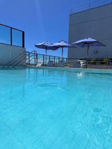 - une piscine d'eau bleue avec des parasols dans l'établissement Flat Novo e Moderno a 200m do Shopping , com Piscina wifii 500mbps, à Récife