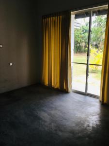een lege kamer met gele gordijnen en een groot raam bij Coconut House in Panadura