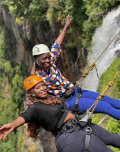 a woman and a girl on a zipline in front of a waterfall at Rock garden Sipi in Kapchorwa