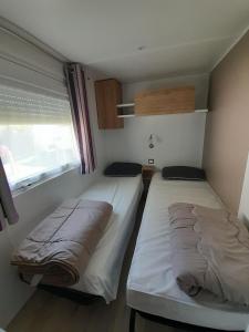 two beds in a small room with a window at Large and comfortable mobile home Clp17 2Ch Siblu Les Charmettes in Les Mathes