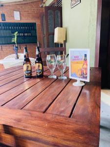 Thal Sewana Home Stay في سيجيريا: زجاجتان من البيرة وكؤوس النبيذ على طاولة خشبية