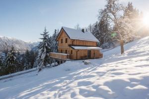 una cabaña de madera en la nieve con el sol detrás de ella en Chalet Jochwand Bad Goisern, en Bad Goisern