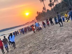 a group of people walking on the beach at sunset at ELLISA HOSPITALITY and SPA in Accra
