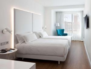 a white bedroom with a bed and a blue chair at NH Madrid Atocha in Madrid