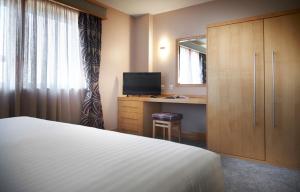 Schlafzimmer mit einem Bett und einem Schreibtisch mit einem Spiegel in der Unterkunft The Suites Hotel & Spa Knowsley - Liverpool by Compass Hospitality in Knowsley