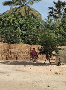 a man riding a motorcycle down a dirt road at Petit Hollande guest rooms in Abémé