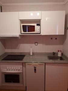 a kitchen with white cabinets and a microwave and a sink at Somo Calle Ria Cubas in Somo