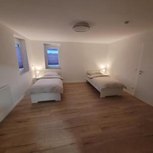 two beds in a white room with wood floors at Apartments am Kochertal in Oedheim