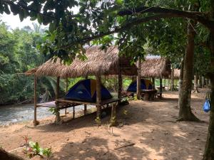 twoiki huts with chairs and tables on a beach at สวนบุศรา ลานกางเต็นท์วิถีเกษตร in Ban Bok Fai