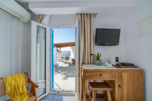 a room with a desk with a television and a balcony at Hotel Madalena in Mikonos