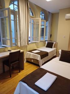 a room with two beds and a desk and windows at Hotel Praça da Matriz in Porto Alegre
