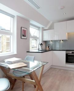 una cocina blanca con mesa de cristal en una habitación en Barbican Serviced Apartments en Londres