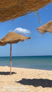 dos sombrillas de paja en una playa con el océano en Luxury villa with a heated indoor pool and direct access to the beach en Nabeul