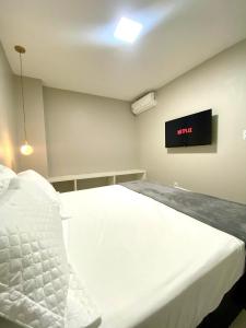 Un dormitorio con una cama blanca y un televisor en la pared. en Casa Amora, en Arraial do Cabo
