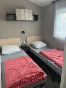 duas camas num pequeno quarto com lençóis vermelhos em Magnifique Mobilhome 3ch-2sdb-Clim Siblu Les Charmettes em Les Mathes