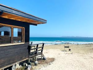 a house on a beach with a bench and the ocean at Punta de Choros Lodge in Punta de Choros