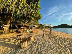 a sandy beach with a bench and a tree at Binucot Lodge in Romblon