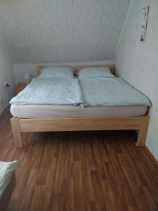 1 cama con sábanas blancas y almohadas en el suelo de madera en Útulná chaloupka v Krkonoších, en Vysoké nad Jizerou