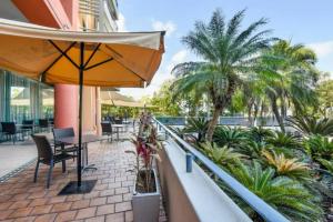 a balcony with an umbrella and chairs and palm trees at Resort Style City View King Bed Pool Balcony in Darwin