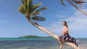 a woman sitting on a palm tree on the beach at S@fe Landing Lodge in Nacula Island