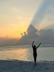a woman standing on the beach with her hands in the air at PrivHotel - Himandhoo in Himandhoo 