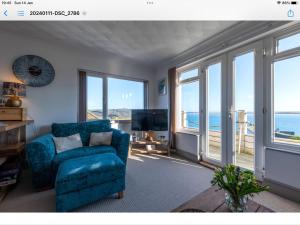 a living room with a blue chair and windows at Lovely 1-Bed Apartment with stunning sea views in Looe