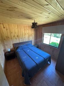 Cama grande azul en habitación de madera con ventana en Cabañas de Montaña Deumayen, en Caburgua