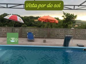 a swimming pool with an umbrella and a chair at Refugio Verde Zen in Dois Vizinhos