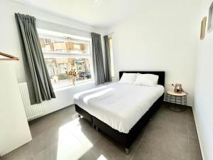 a white bedroom with a bed and a window at Family apartment on the ground floor with terrace - Panne A Côte in De Panne