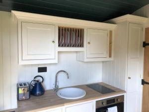 a kitchen counter with a sink and white cabinets at The Old Vicarage Shepherd's Hut in Stroud