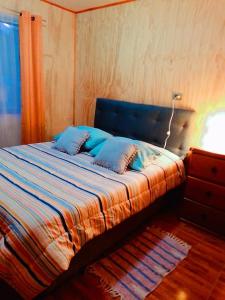a bed with blue pillows in a bedroom at Tu cabaña en paraíso termal in Liquiñe