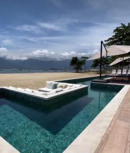 einen Pool mit weißer Couch vor einem Strand in der Unterkunft Ágape Suítes & Apartamentos in São Sebastião