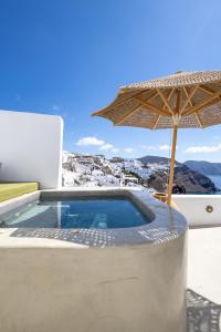 a swimming pool with an umbrella and a table at Rhenia's Suites in Oia