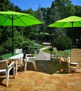 un patio con mesas, sillas y sombrillas verdes en BALATON ART Guesthouse, en Balatonszemes