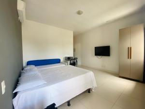 ein Schlafzimmer mit einem weißen Bett und einem Fernseher in der Unterkunft Suíte privativa próxima ao Sesc 1 in Bertioga