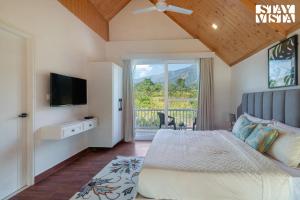 1 dormitorio con cama, TV y balcón en StayVista at SilverSpring Cottage with Valley View & Bonfire en Dehradun