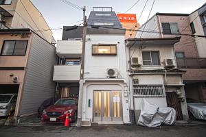 a white house with a door and a car parked in front at - UMI-Haven 福島 - 隣駅5LDK戸建 in Osaka