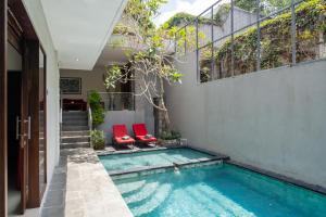 a swimming pool with two red chairs next to a building at Affordable villa @Nyanyi, near Tanah Lot Temple in Munggu