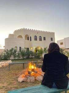 a woman sitting on a bench in front of a fire at Dar Oueghlani - Maison d'hôtes in El Mây
