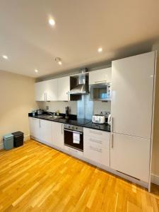 a kitchen with white cabinets and a wooden floor at Contemporary 2BD Flat wBalcony Canary Wharf! in London