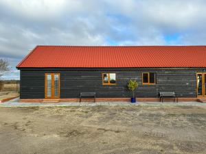 uma pequena casa com um telhado vermelho e dois bancos em Brooke View Barns No 1 em Norwich