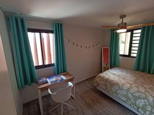 1 dormitorio con escritorio y 1 cama con cortinas verdes en Ravissante maison sur les hauteurs, en Faaa