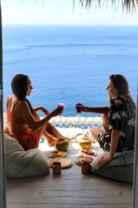 due donne sedute intorno a un tavolo con cibo e bevande di Tropical Glamping Nusa Penida Diamond Beach - Cliff Side Edge a Nusa Penida